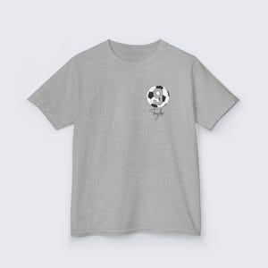 May include: Gray t-shirt with a black and white soccer ball graphic with the number 9 on it. The text "Taylor" is written below the ball.
