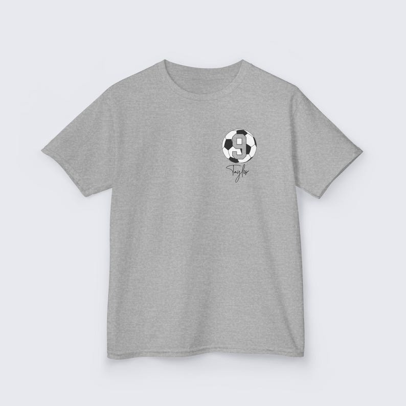 May include: Gray t-shirt with a black and white soccer ball graphic with the number 9 on it. The text "Taylor" is written below the ball.