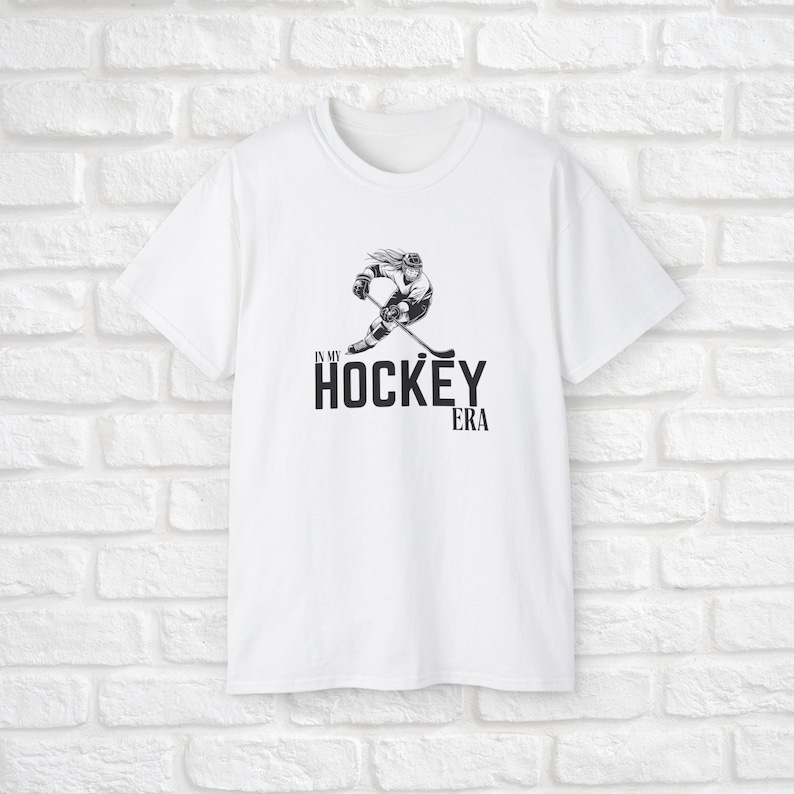Puede incluir: Camiseta blanca con una ilustraci&oacute;n en blanco y negro de un jugador de hockey y el texto "In My Hockey Era".