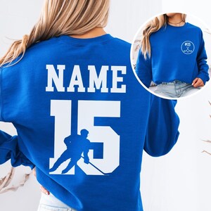 Custom hockey sweatshirt featuring a personalized hockey player name and number design on the back as well as jersey number on the front design.  Also, choose from a variety of hockey player silhouettes to further customize this hockey sweater