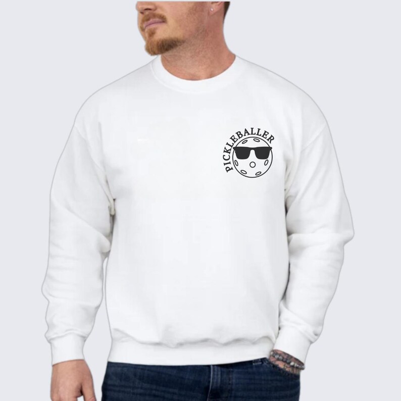 May include: White sweatshirt with a black graphic of a pickleball with sunglasses and the text "Pickleballer".