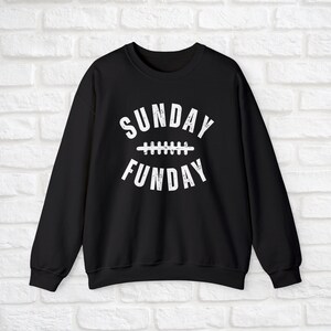 Op de afbeelding: Zwart sweatshirt met witte tekst die "SUNDAY FUNDAY" luidt met een voetbalnaadgrafiek tussen de woorden.