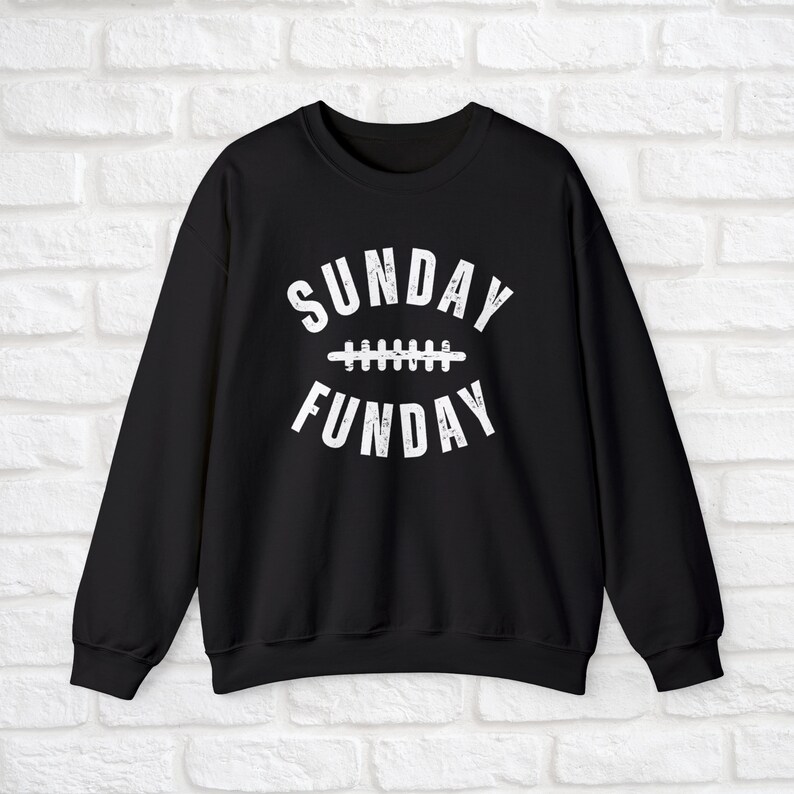 Op de afbeelding: Zwart sweatshirt met witte tekst die "SUNDAY FUNDAY" luidt met een voetbalnaadgrafiek tussen de woorden.