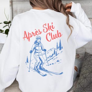 May include: White sweatshirt with a blue and red graphic of a skier on a mountain with the text "Apres Ski Club".