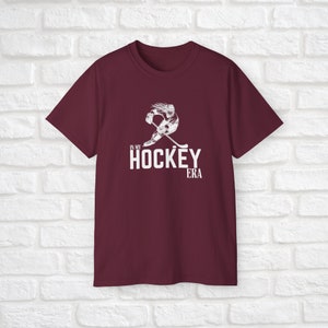 Puede incluir: Camiseta color burdeos con un gr&aacute;fico blanco de un jugador de hockey patinando con un palo y el texto "In My Hockey Era".