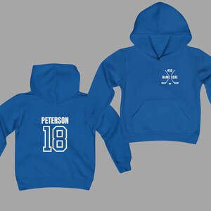 May include: Two blue hoodies. One displays "PETERSON" and the number "18" in white block letters on the back. The other hoodie has a hockey stick and puck graphic with the number "18" and space for a name. Both have a hood and a front pocket.