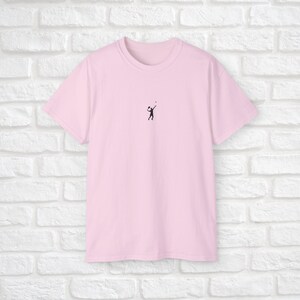 Pu&ograve; includere: Una maglietta rosa con una piccola silhouette nera di una persona che gioca a pallavolo sul davanti.