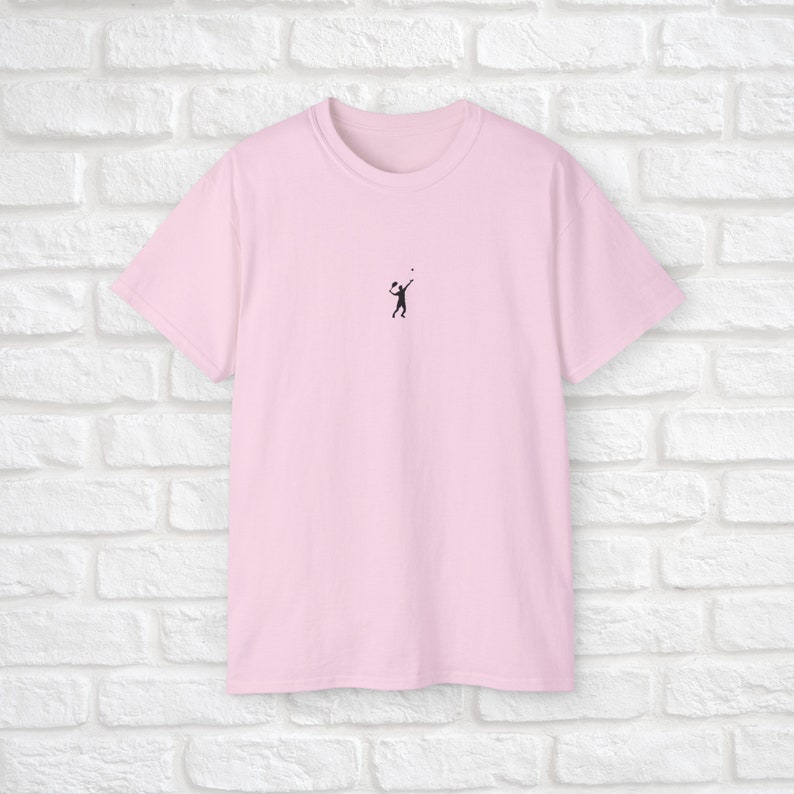 Pu&ograve; includere: Una maglietta rosa con una piccola silhouette nera di una persona che gioca a pallavolo sul davanti.