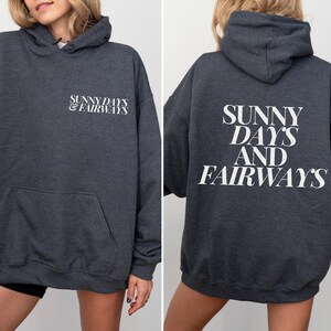 dark heather golf themed hoodie with sunny days and fairways in a bold, trendy font on the back of the shirt. On the front, is a small sunny days and fairways graphic on the left chest
