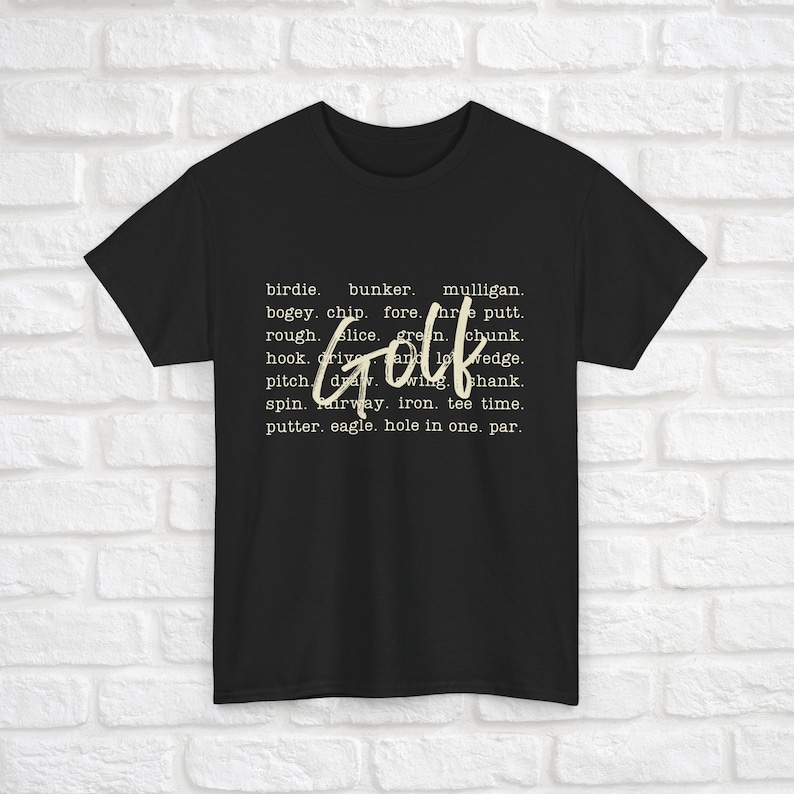 K&ouml;nnte beinhalten: Schwarzes T-Shirt mit dem Wort "Golf" in gro&szlig;en wei&szlig;en Buchstaben. Das Wort ist von einer Liste von Golfbegriffen in kleineren wei&szlig;en Buchstaben umgeben.