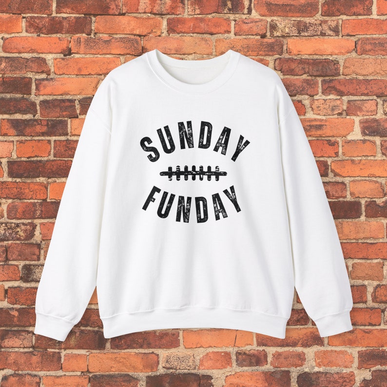 Op de afbeelding: Wit sweatshirt met een zwarte grafische afbeelding die "SUNDAY FUNDAY" zegt met een voetbalnaadontwerp in het midden.