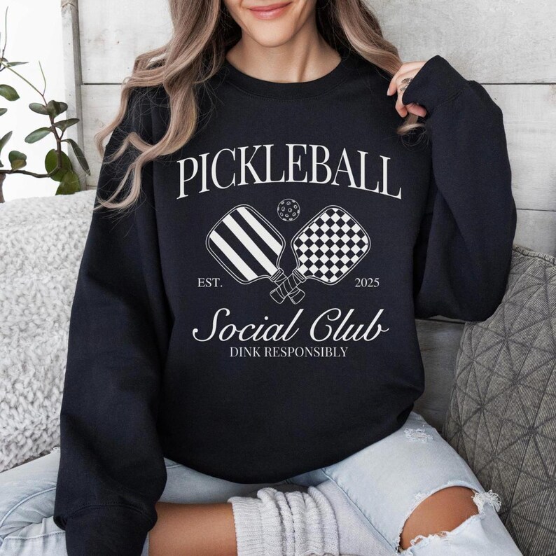 Puede incluir: Sudadera negra con texto blanco que dice "Pickleball Social Club Est. 2023 Dink Responsibly" y un gr&aacute;fico de dos palas de pickleball.