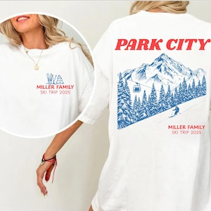 May include: White t-shirt with a ski trip design. The front has a small graphic with skis and trees, and the text "MILLER FAMILY SKI TRIP 2025." The back displays "PARK CITY" in red, a mountain scene, and the same text.