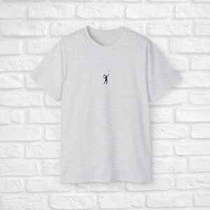 Pu&ograve; includere: Una t-shirt grigia melange con una piccola silhouette nera di una persona che gioca a pallavolo sul davanti.