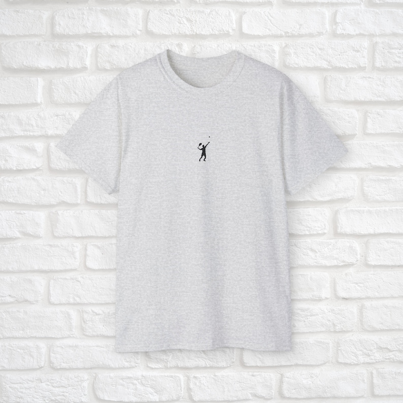 Pu&ograve; includere: Una t-shirt grigia melange con una piccola silhouette nera di una persona che gioca a pallavolo sul davanti.