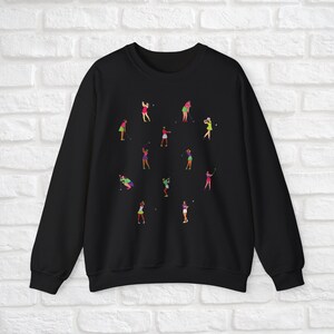 May include: Black sweatshirt featuring a colourful graphic print of women playing golf. The design depicts multiple women in different poses, holding golf clubs and balls.