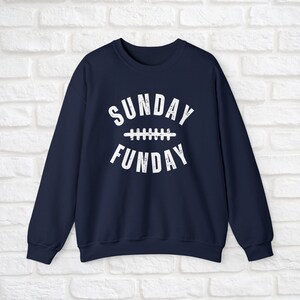 Op de afbeelding: Donkerblauwe trui met witte tekst die "SUNDAY FUNDAY" luidt met een voetbalnaadgrafiek tussen de woorden.