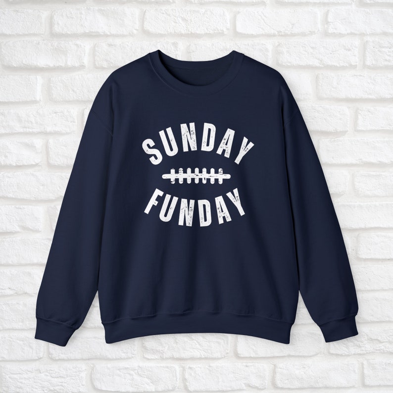 Op de afbeelding: Donkerblauwe trui met witte tekst die "SUNDAY FUNDAY" luidt met een voetbalnaadgrafiek tussen de woorden.
