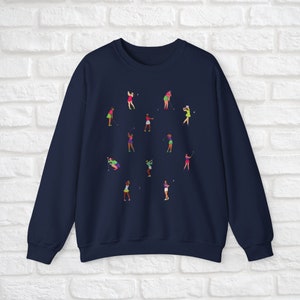 May include: Navy blue sweatshirt featuring a design of women playing golf in different poses. The women are wearing colourful clothing and holding golf clubs.