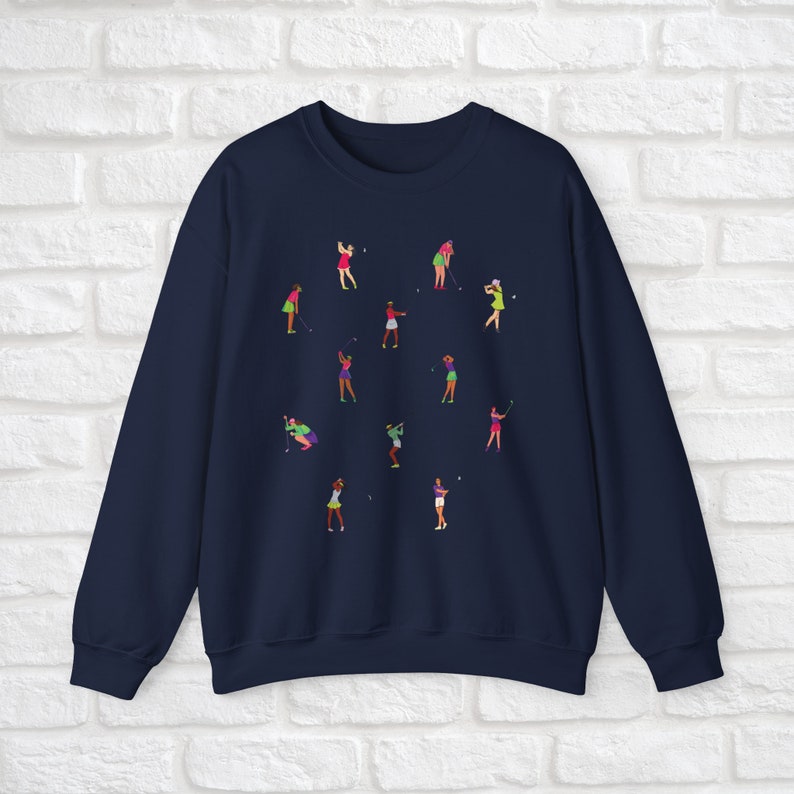 May include: Navy blue sweatshirt featuring a design of women playing golf in different poses. The women are wearing colourful clothing and holding golf clubs.