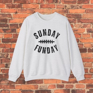 Op de afbeelding: Een lichtgrijs sweatshirt met de tekst "SUNDAY FUNDAY" in zwart, met een voetbalafbeelding tussen de woorden.
