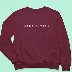 May include: Burgundy sweatshirt with the text "MAKE PUTTS" in white.