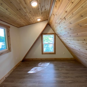 May include: A room with a sloped ceiling and wood paneling. There are two windows, one on each side of the room. The floor is a light brown wood.