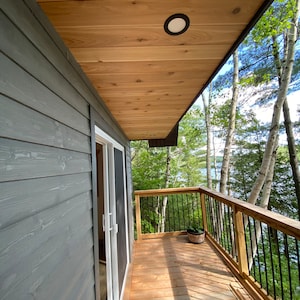 May include: A wooden deck with a railing overlooking a wooded area. The deck has a wooden ceiling with a light fixture. A door leads to the interior of the house.
