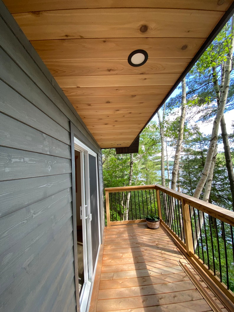 May include: A wooden deck with a railing overlooking a wooded area. The deck has a wooden ceiling with a light fixture. A door leads to the interior of the house.