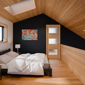 Puede incluir: Un dormitorio moderno con una pared de acento negra, techo de madera y pisos de madera. Una cama con ropa de cama blanca y una almohada a rayas est&aacute; en primer plano. Una pintura abstracta con tonos rojos y azules cuelga de la pared. Se ve una puerta con paneles de vidrio esmerilado.