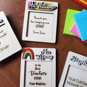 May include: Four wooden frames with personalized messages for teachers. Each frame has a different design element, including a pencil, rainbow, and a heart. The frames are blank inside for writing a message.