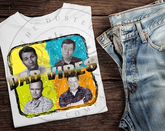 May include: White t-shirt with a graphic design featuring four men's faces and the text "DAD VIBES". The graphic is in a yellow, blue, and orange color scheme with a grunge effect.
