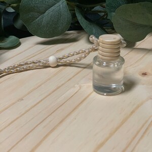 May include: A clear glass bottle with a wooden cap and a beige cord with a white bead. The bottle is sitting on a light wood surface.