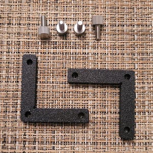 May include: Two black plastic corner brackets with four screw holes each. The brackets are designed to be used for joining two pieces of wood or other materials at a 90-degree angle. Four silver screws are included.