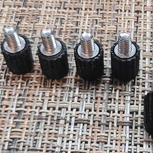 May include: A close-up of eight black and silver screws with a textured finish. The screws are arranged in a row on a woven surface.