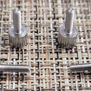 May include: Four silver thumbscrews with a knurled head and a threaded shaft. The thumbscrews are arranged in two pairs, with the heads facing each other.