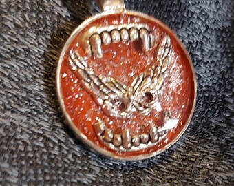 round pendant with a spooky mask inside vampire teeth salmon glitter