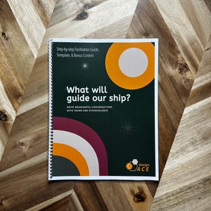 May include: A spiral-bound booklet with a dark green cover featuring the title "What will guide our ship?" and the text "Step-by-step Facilitation Guide, Template, & Bonus Content." The cover also includes orange and white geometric shapes and the "design ACE" logo.
