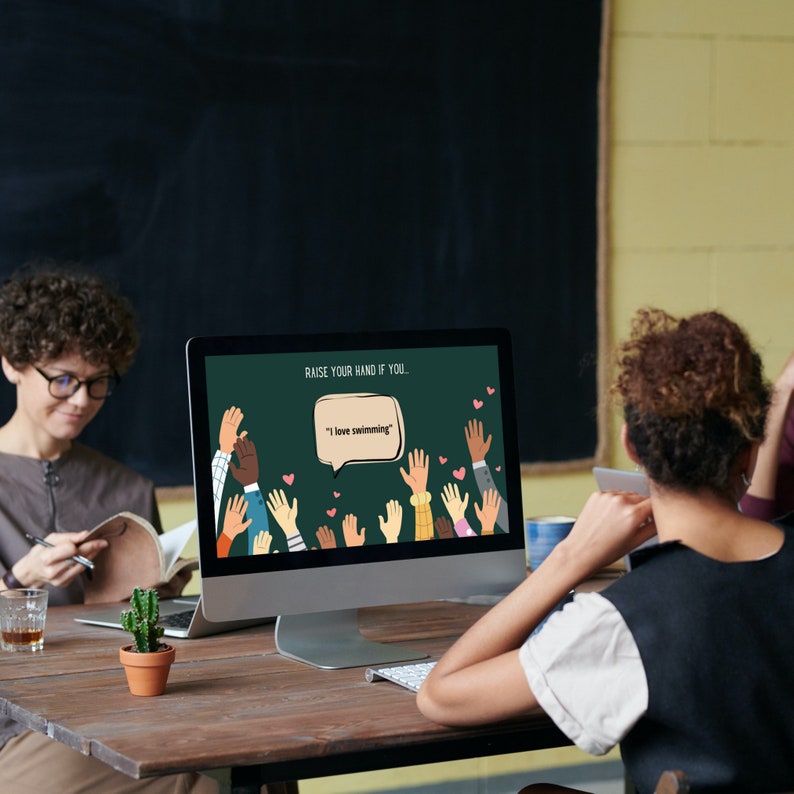 Colleagues participating in a 'Raise Your Hand If You' game, with the prompt 'I love swimming' displayed on a computer screen.