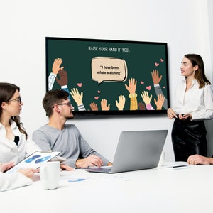 Team participating in a 'Raise Your Hand If You' activity for the That's Me icebreaker during a meeting, with the prompt 'I have been whale watching' displayed on a screen.