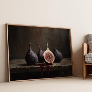 May include: A framed painting depicting three purple figs on a dark brown surface. The figs are arranged in a row, with one fig cut in half, revealing its red flesh. The painting is set against a light beige wall.