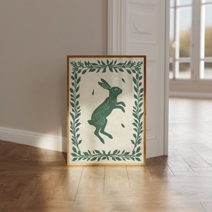May include: A green silhouette of a rabbit jumping inside a leafy green frame on a cream background.