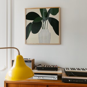 May include: A framed art print featuring a stylized illustration of a plant with large, dark green leaves in a striped vase. The artwork hangs above a wooden cabinet with a yellow lamp, amplifier, and electronic music equipment.