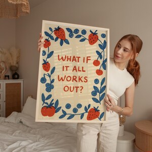 K&ouml;nnte beinhalten: Ein gerahmter Kunstdruck mit dem Text "WHAT IF IT ALL WORKS OUT?" umgeben von Illustrationen von Erdbeeren, Blaubeeren und Bl&auml;ttern. Das Kunstwerk hat einen cremefarbenen Hintergrund und einen hellen Holzrahmen.