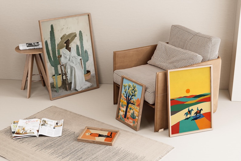Op de afbeelding: Verschillende ingelijste kunstdrukken, waaronder woestijnlandschappen en een portret, worden gepresenteerd in de buurt van een stoel. Een print toont een persoon in een witte jurk en hoed met cactussen. Andere prints tonen woestijnsc&egrave;nes met ruiters.