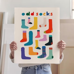 Puede incluir: Un póster con las palabras "odd socks" en letras coloridas. El póster presenta una colección de calcetines desparejados en varios colores y patrones, incluyendo rayas y colores lisos. Los calcetines están dispuestos en un patrón de cuadrícula.
