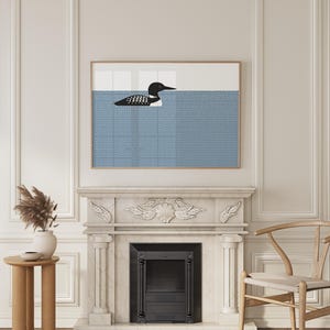 May include: A framed art print featuring a stylized black and white loon swimming in blue water. The water has a dotted pattern. The artwork is displayed above a fireplace with a white mantel and a black firebox.