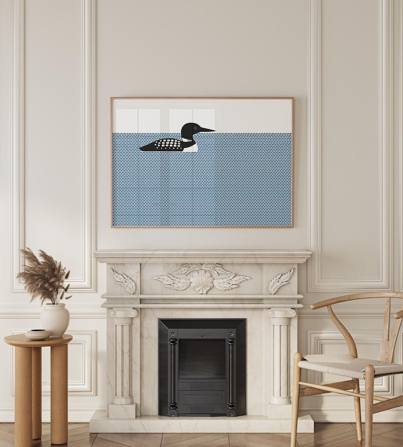 May include: A framed art print featuring a stylized black and white loon swimming in blue water. The water has a dotted pattern. The artwork is displayed above a fireplace with a white mantel and a black firebox.