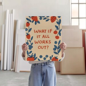 K&ouml;nnte beinhalten: Ein rechteckiger Kunstdruck mit dem Text "WHAT IF IT ALL WORKS OUT?" umrahmt von Illustrationen von Erdbeeren, Blaubeeren und Bl&auml;ttern. Der Druck wird vor einer Person gehalten, die ein wei&szlig;es Hemd und blaue Jeans tr&auml;gt.