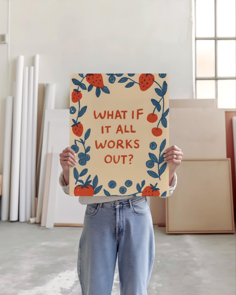 K&ouml;nnte beinhalten: Ein rechteckiger Kunstdruck mit dem Text "WHAT IF IT ALL WORKS OUT?" umrahmt von Illustrationen von Erdbeeren, Blaubeeren und Bl&auml;ttern. Der Druck wird vor einer Person gehalten, die ein wei&szlig;es Hemd und blaue Jeans tr&auml;gt.